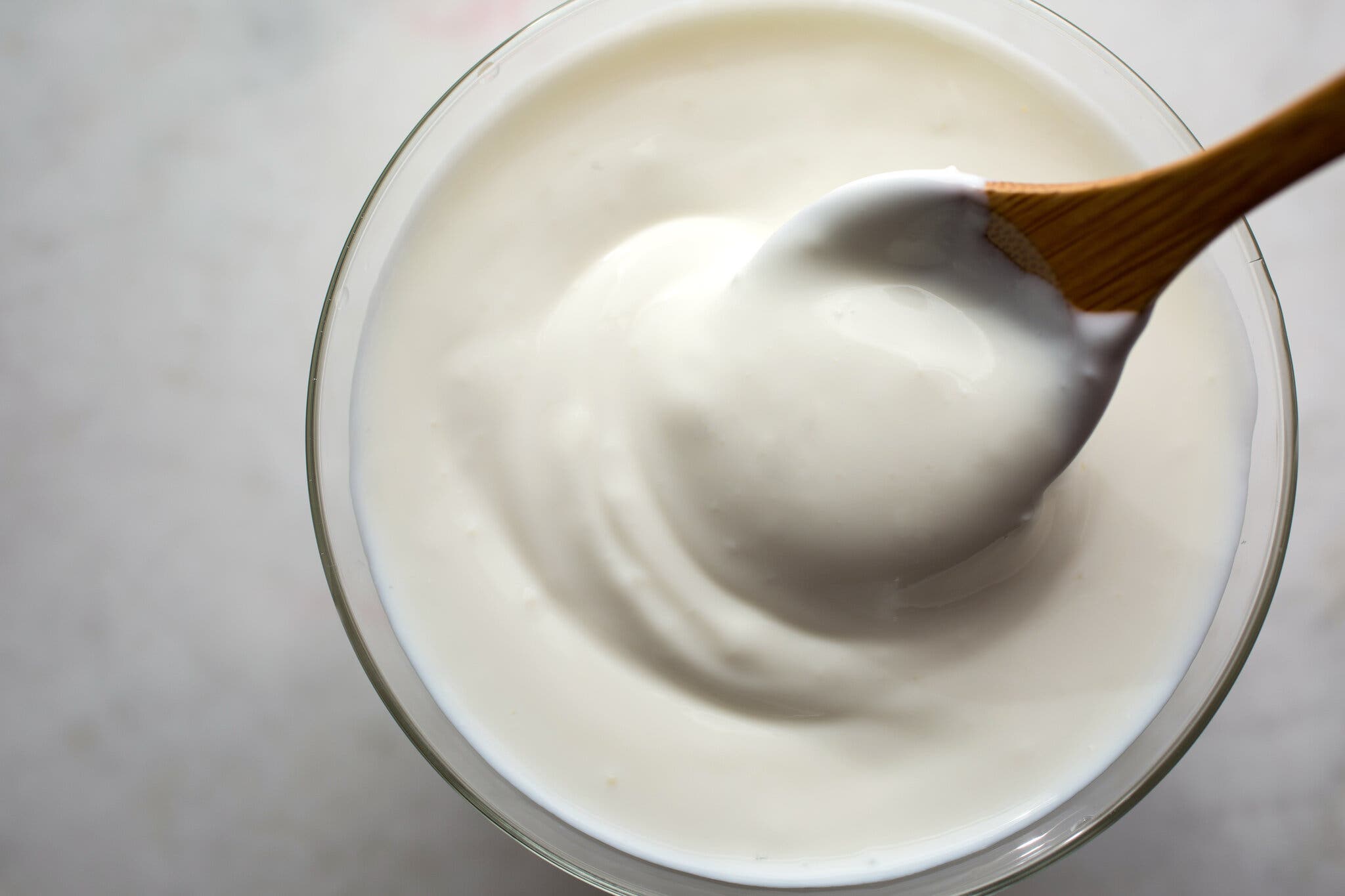 An overhead image of a bowl of yogurt. A wooden spoon pulls out a small scoop.