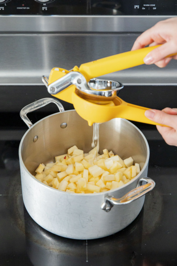 Squeezing lemon juice into a stainless saucepan filled with chopped apples.