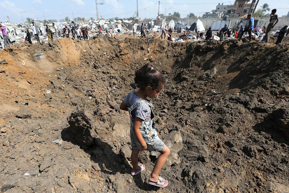 A displaced Palestinian girl walks next to an impact crater, left behind after an Israeli strike, at a camp for internally displaced people in Deir el-Balah in the central Gaza Strip (AFP/Getty)