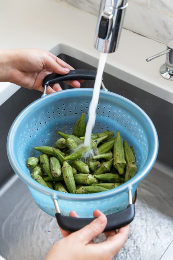 Washing fresh green okra in a collander in the sink.