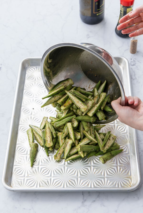 Dumping seasoned okra onto an oiled baking sheet before baking.