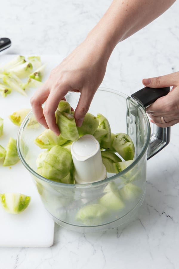 Placing coarsely chopped, cored green tomatoes in a food processor.