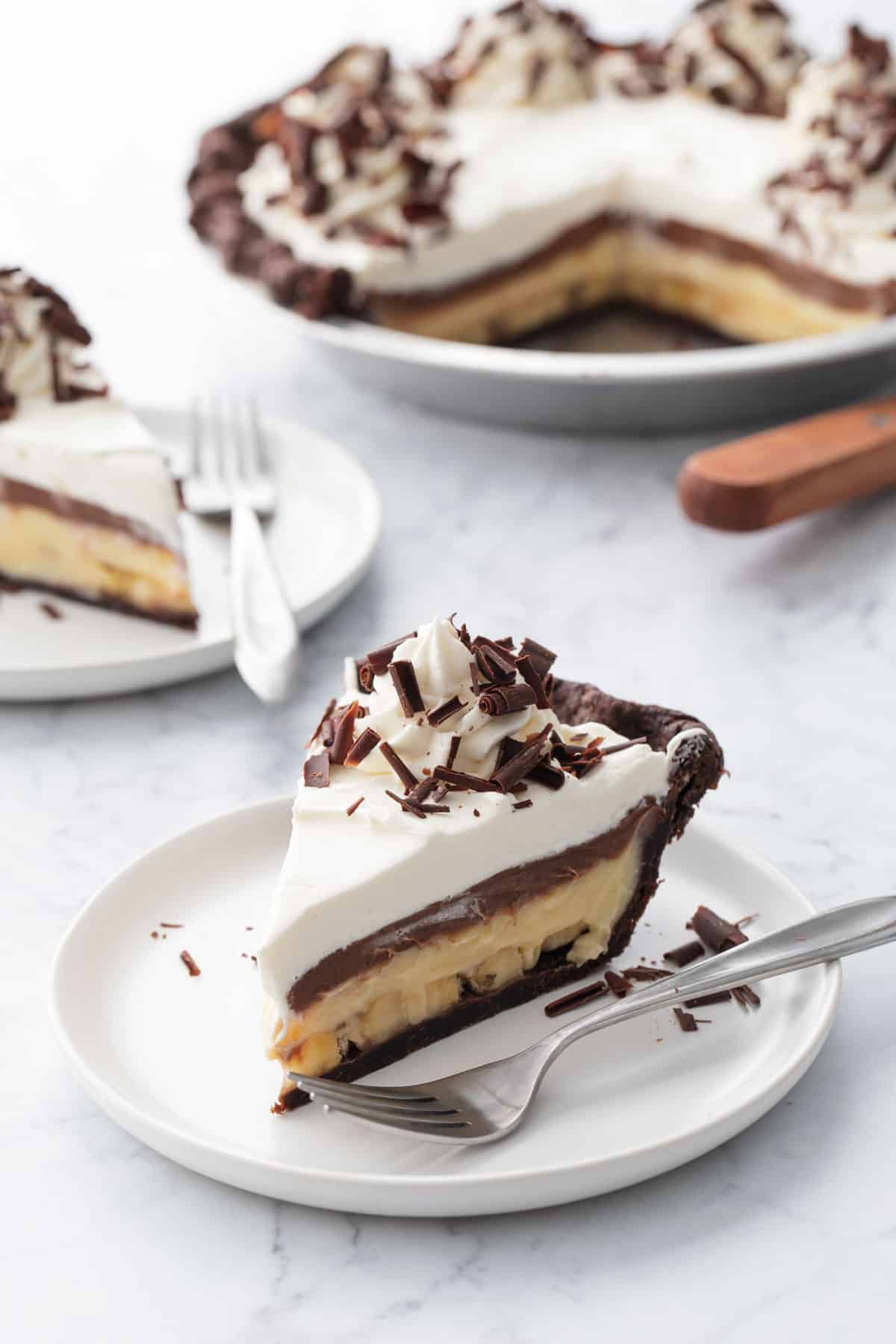 Chocolate Banana Cream Pie with Flaky Chocolate Pie Crust sliced on white plates on marble background.
