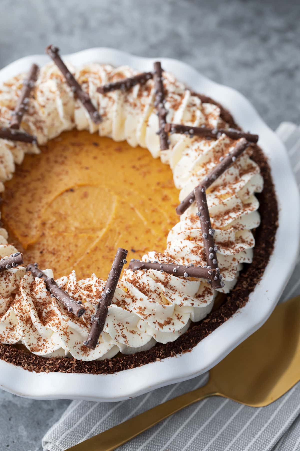 Black Bottom Pumpkin Cream Pie topped with a border of piped whipped cream, grated chocolate, and chocolate sticks for garnish.