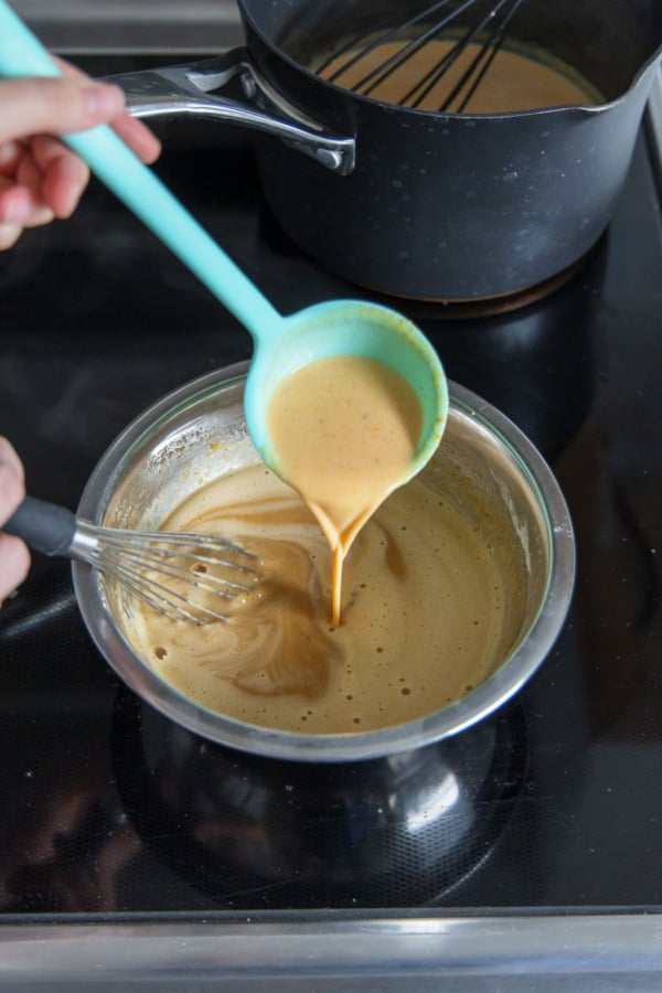Ladling hot milk mixture into bowl with egg yolks to temper.