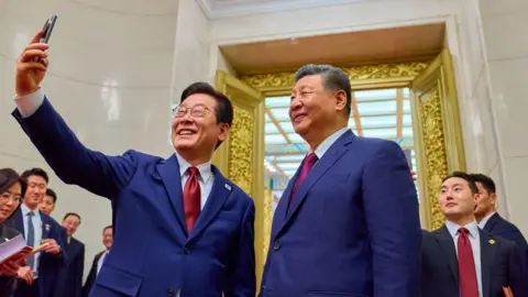 EPA/Shutterstock Lee Jae Myung and Xi, both wearing navy suits and red ties, taking a selfie together.