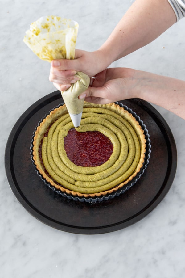 Piping a spiral of green frangipane filling on top of the raspberry jam layer in the crust.