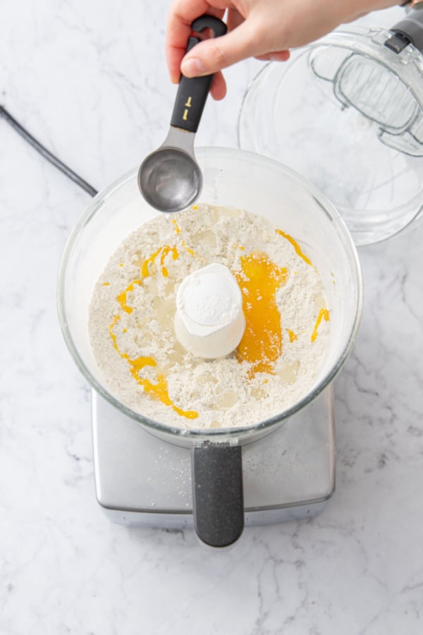 Adding egg yolk and ice water to shortcrust mixture in the food processor.