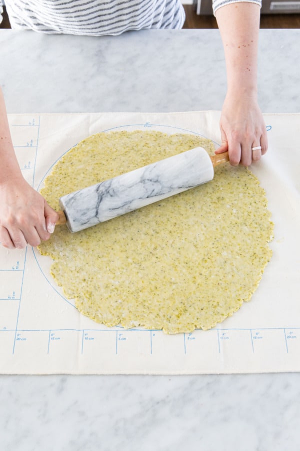 Rolling out pistachio tart crust dough on a flour-dusted pastry cloth.
