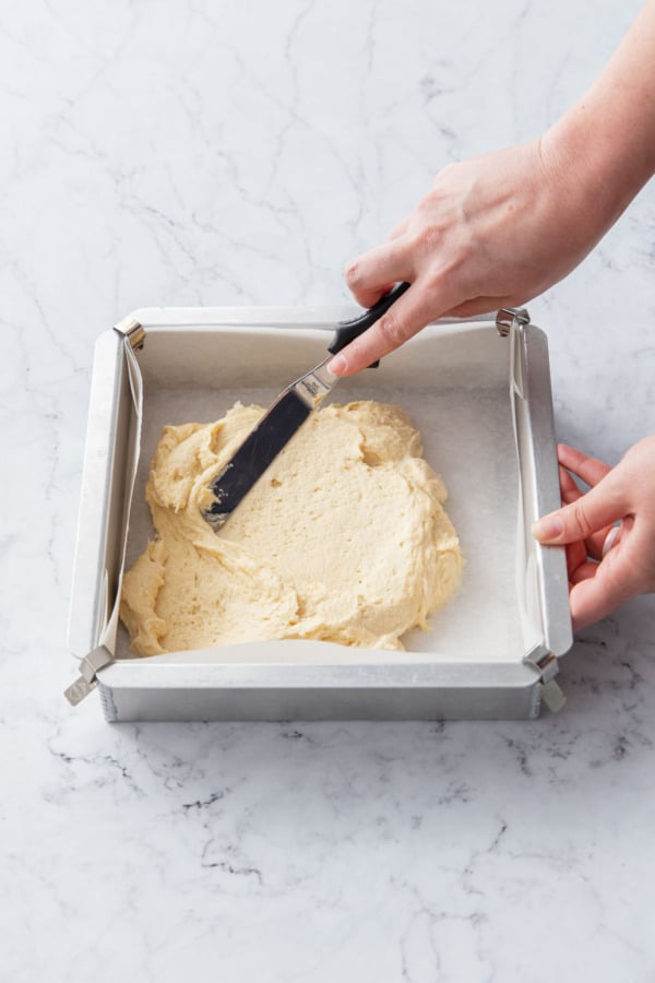 Spreading cake batter into a square baking pan using an offset spatula.