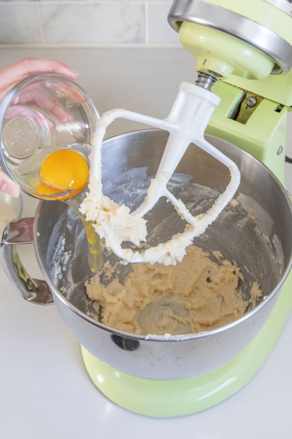 Adding an egg to a stand mixing bowl with creamed butter and sugar.