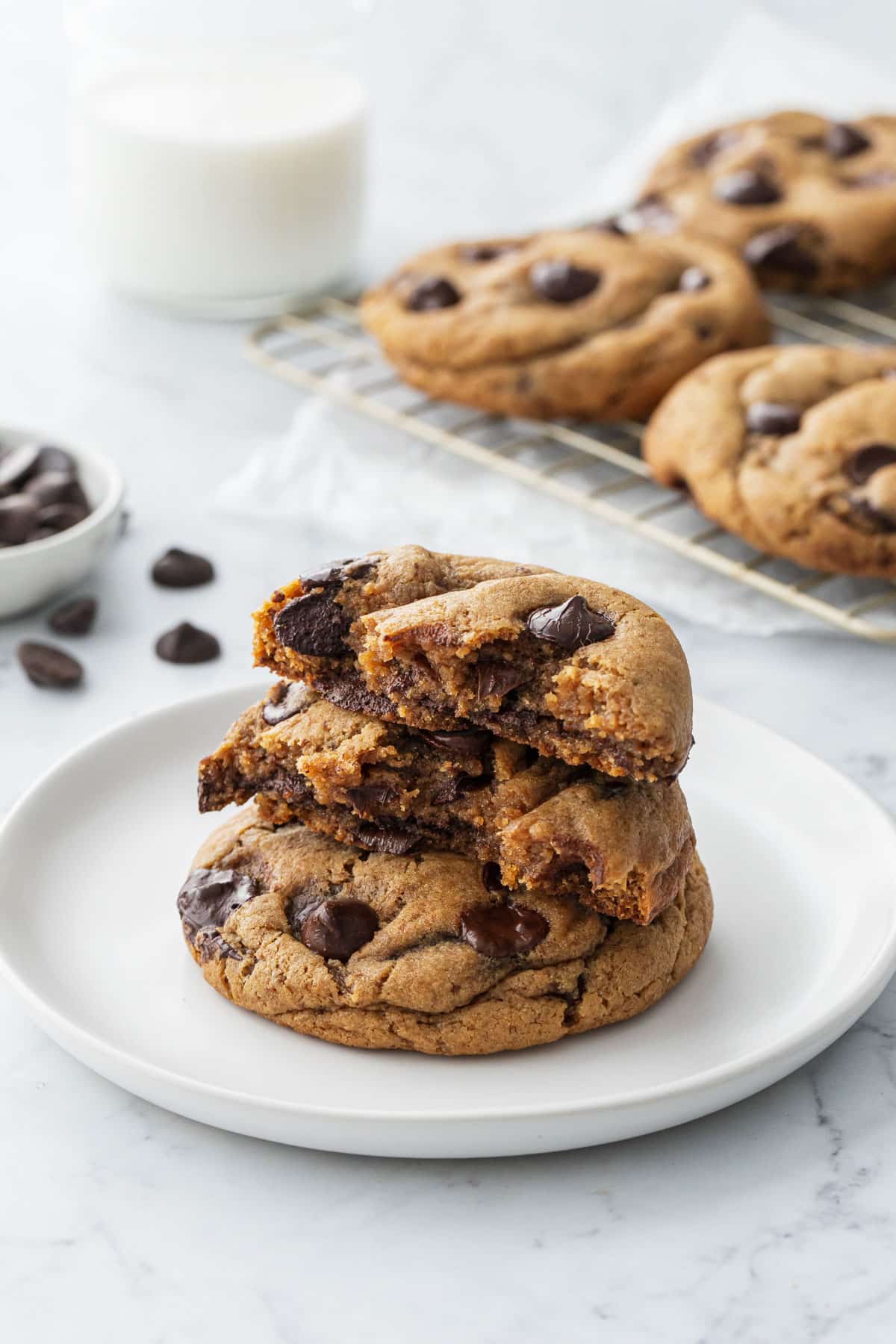 Stack of Brown Butter Chocolate Chip Cookies on a white plate, one cookie split in half to show the gooey interior texture.