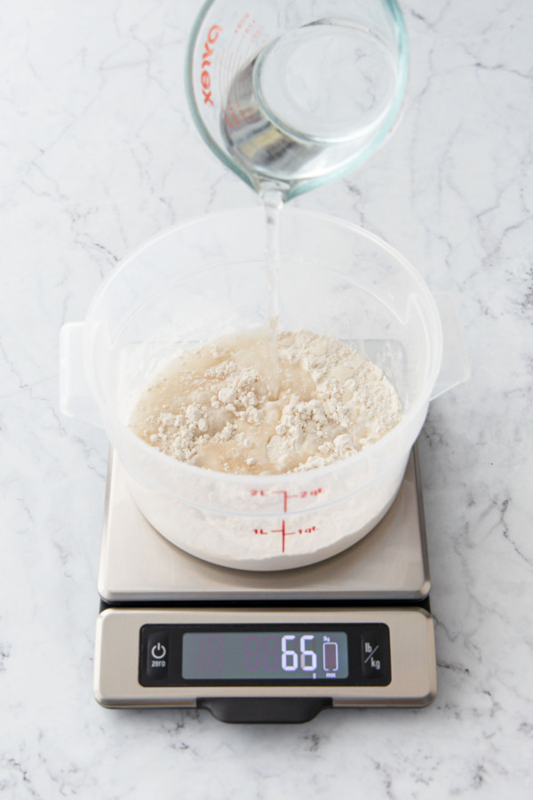 Pouring water into a container with flour and yeast on a kitchen scale.
