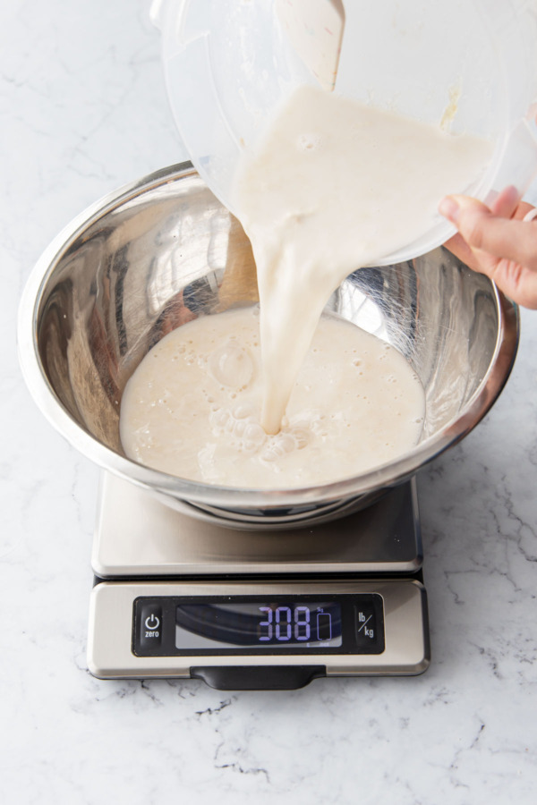 Pouring the well-mixed poolish mixture into a large metal mixing bowl.