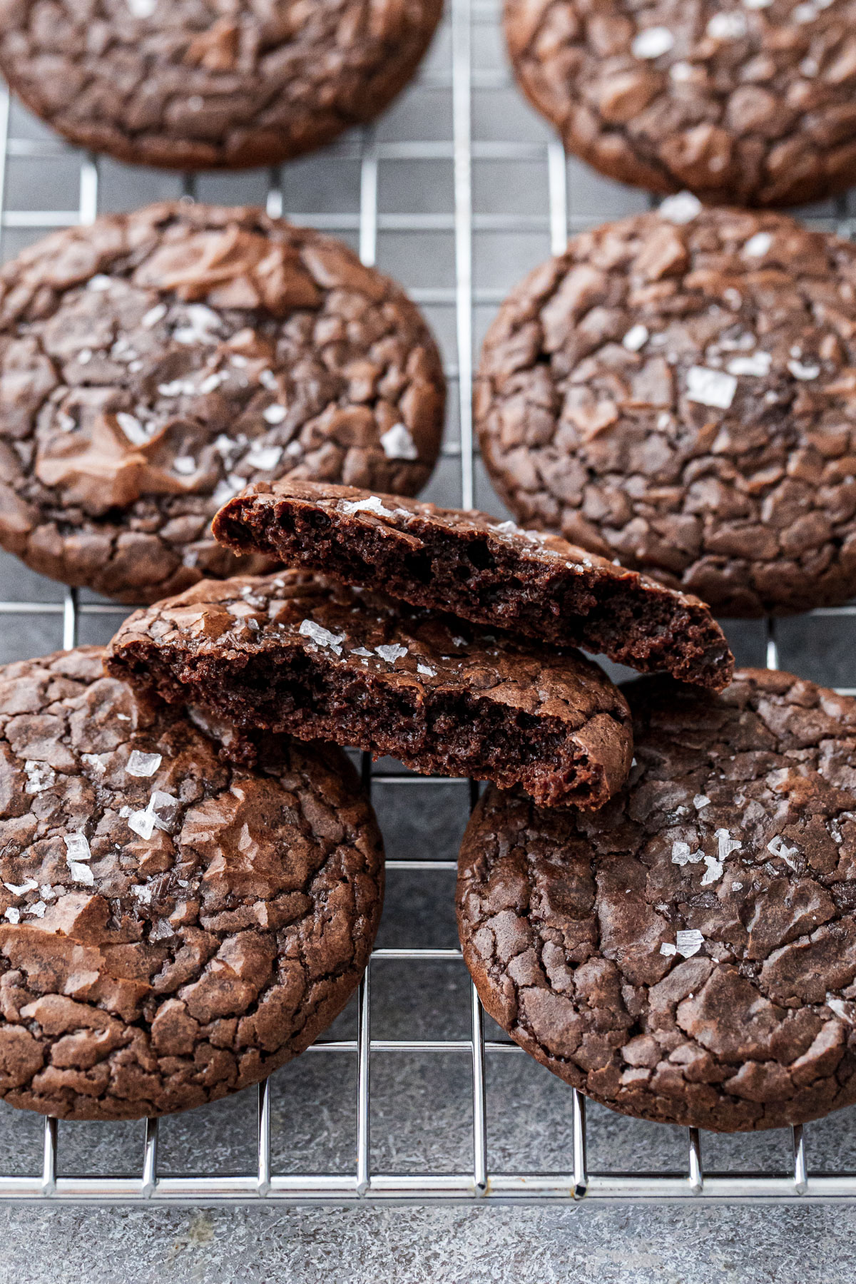 Chewy Crinkle-Top Brownie Cookies on a wire baking rack, one cookie broken in half to show the fudgy interior texture.