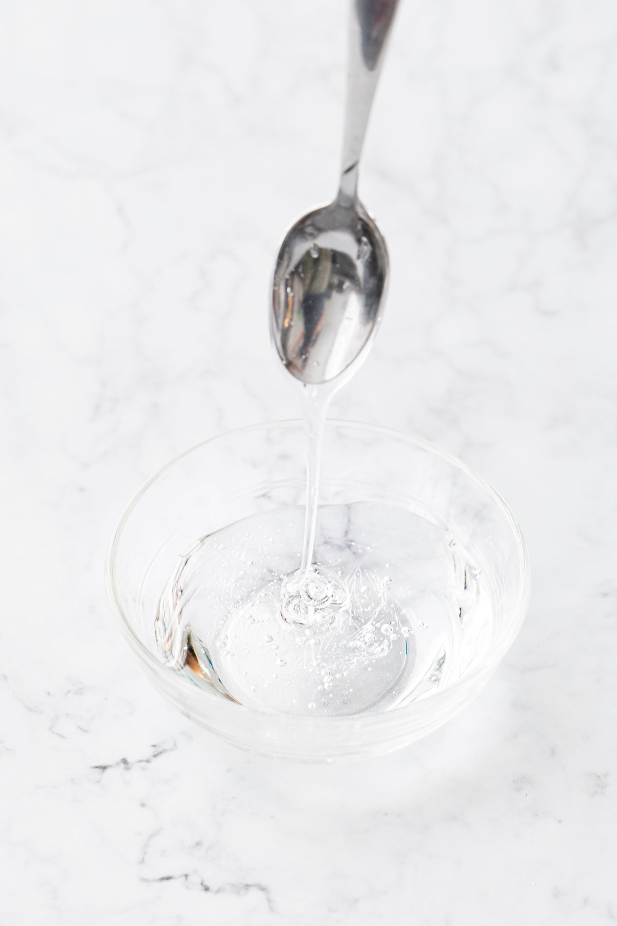 Clear bowl filled with glucose syrup, a spoon drizzling the syrup to show texture and thickness.