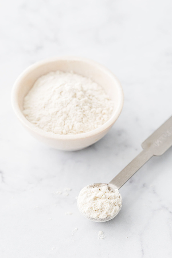 White bowl with powdered guar gum, with a quarter teaspoon of guar gum on the side.