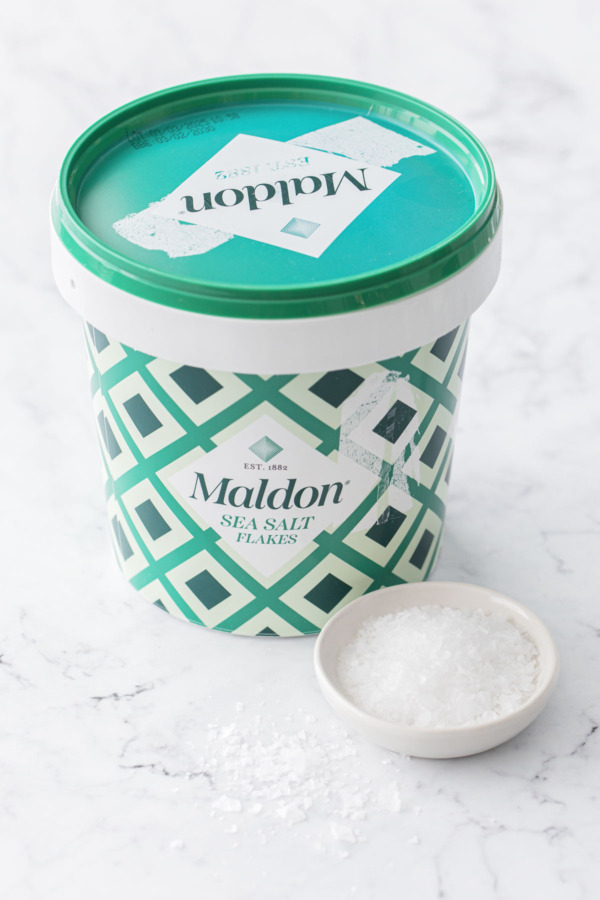 Bucket of Maldon sea salt with a small bowl of salt and some salt scattered around.