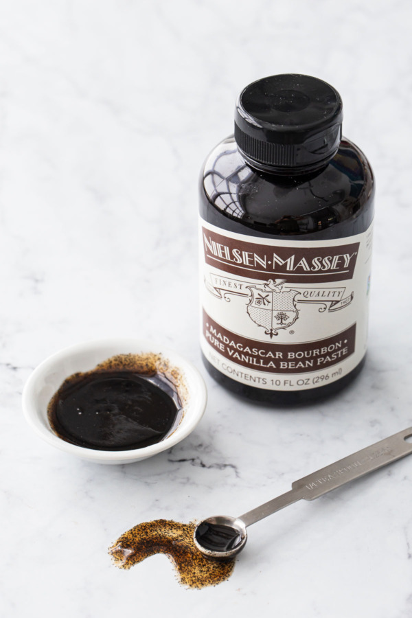 Bottle of vanilla bean paste with a small bowl and measuring spoon on the side.