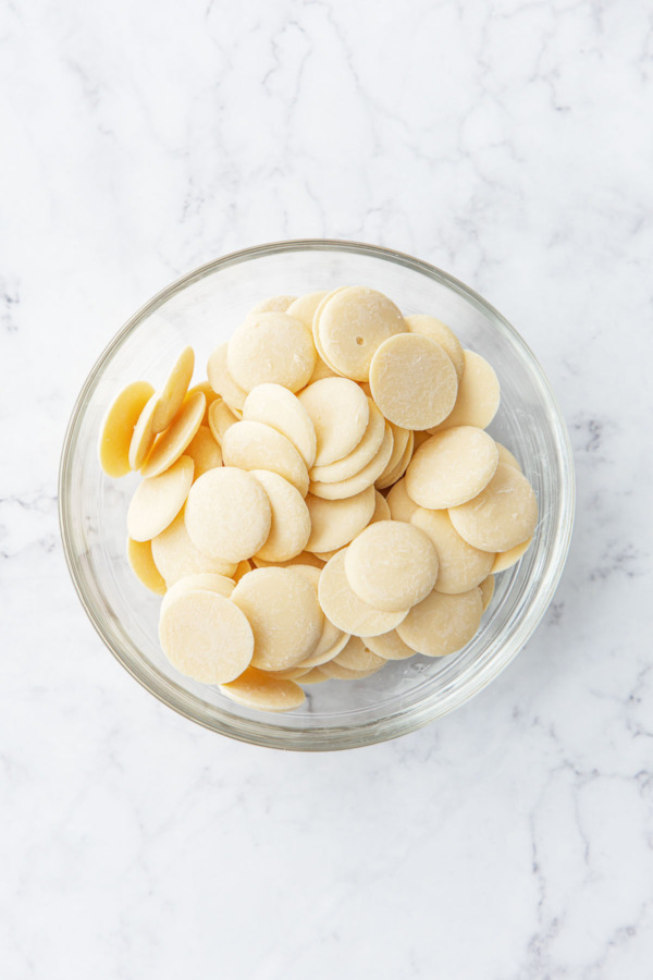 Bowl of white chocolate coverture chocolate on a white marble background.