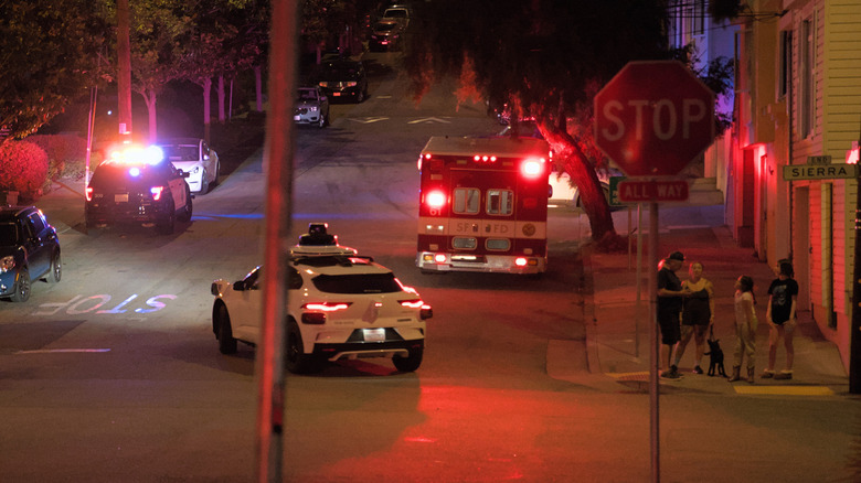 A Waymo navigates a residential street crossing an emergency scene and driving between emergency response vehicles.