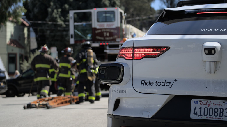 Firefighters work on responding to a fire while a Waymo car drives through the emergency scene.