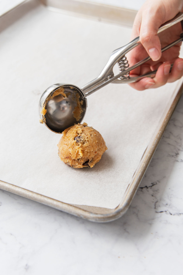 Dropping cookie dough ball onto a parchment-lined baking sheet.