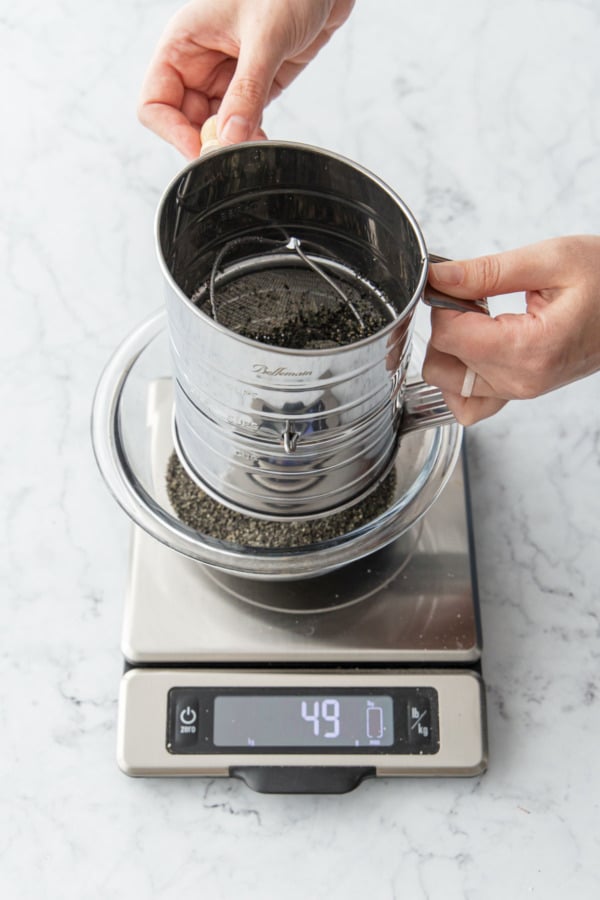 Sifting finely ground black sesame powder into a mixing bowl on a scale.