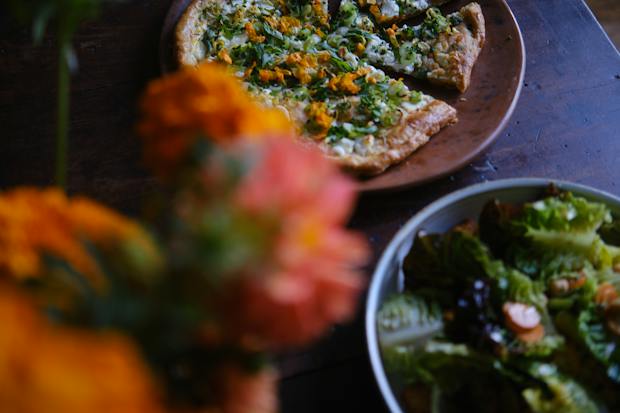 goat cheese tart served on a wood table with flowers and a salad