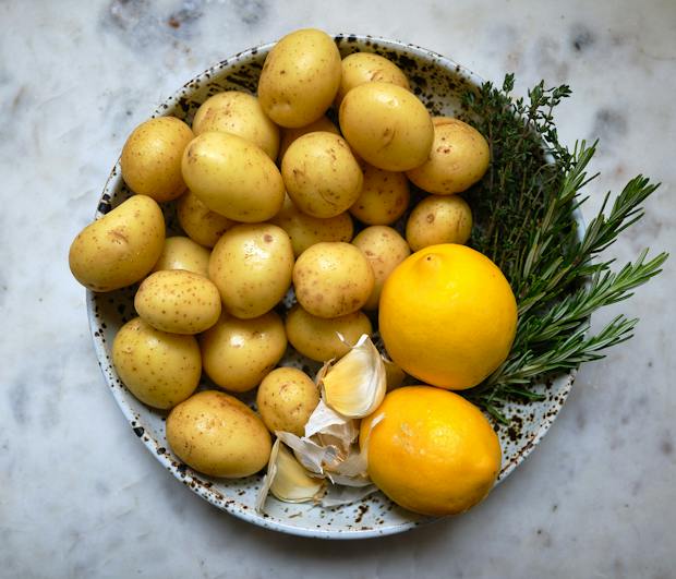Ingredients for lemon roasted potatoes in a bowl including garlic thyme and rosemary