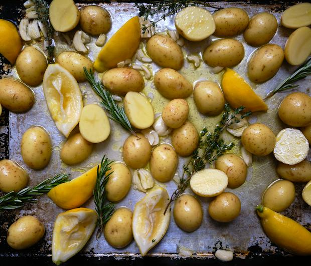 Ingredients for lemon roasted potatoes on a sheetpan and tossed with olive oil before baking