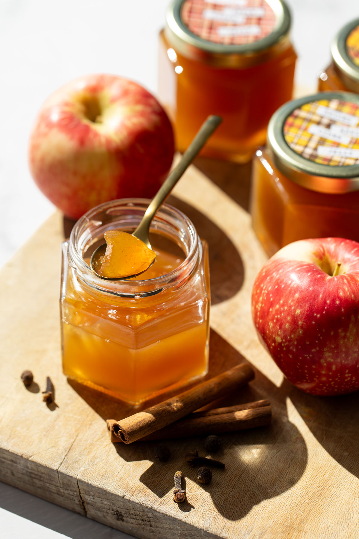 Jar of Spiced Apple Cider Jelly on a wooden board, with a spoonful of jelly resting on top to show the glass-like appearance and texture.