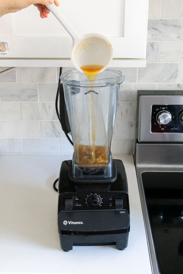 Ladling some of the hot cider into a blender.
