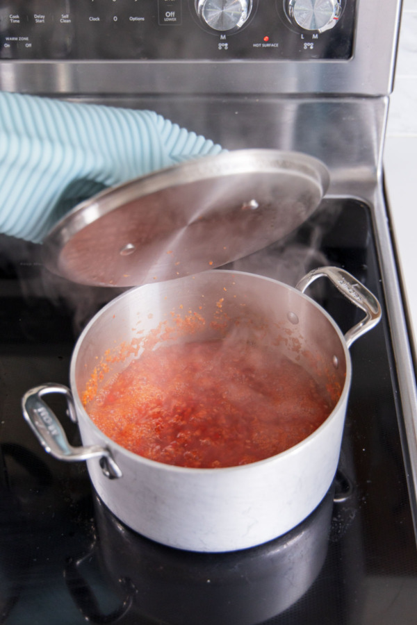 Covering saucepan filled with simmering peppers and vinegar.