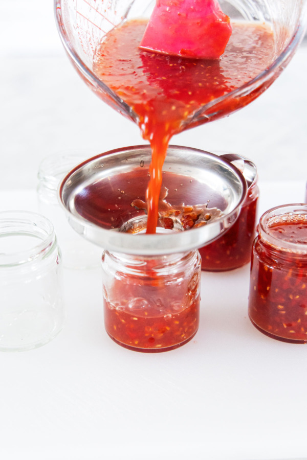 Pouring cooked pepper jelly mixture into clean sterilized canning jars.